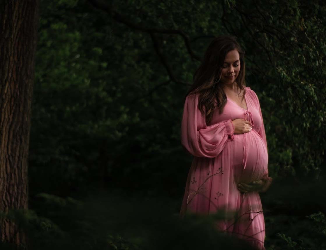 Pregnant woman with a pink dress on the forest